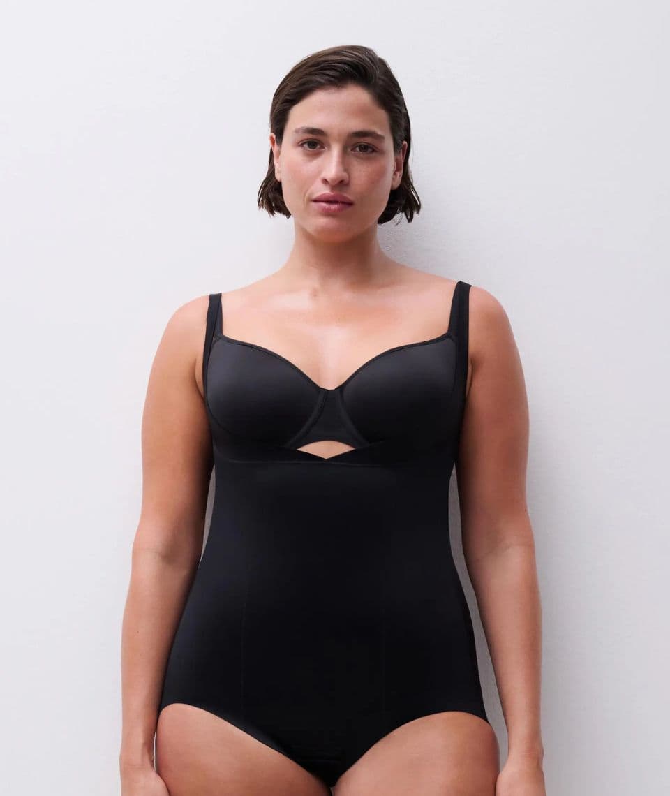 Person wearing a black one-piece swimsuit with a small cutout under the bust, standing against a plain white background.