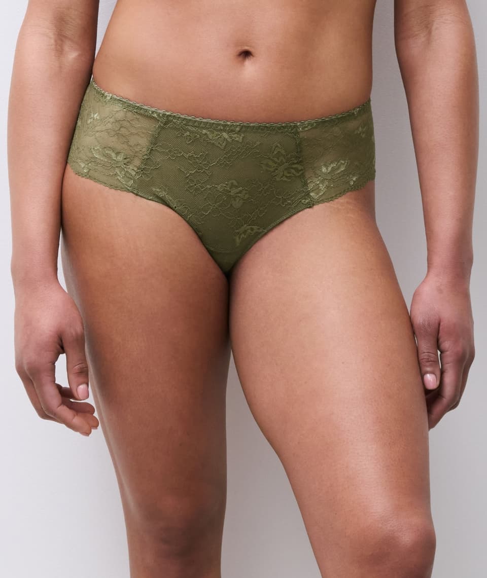 Person wearing olive green lace underwear, standing against a light gray background.