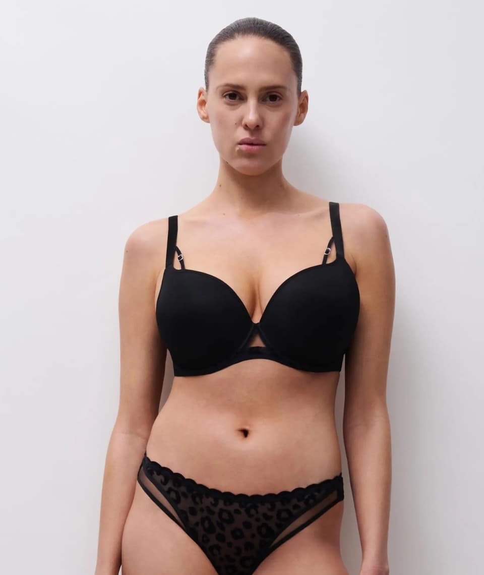 Person wearing a black bra and leopard print panties, standing against a plain white background.