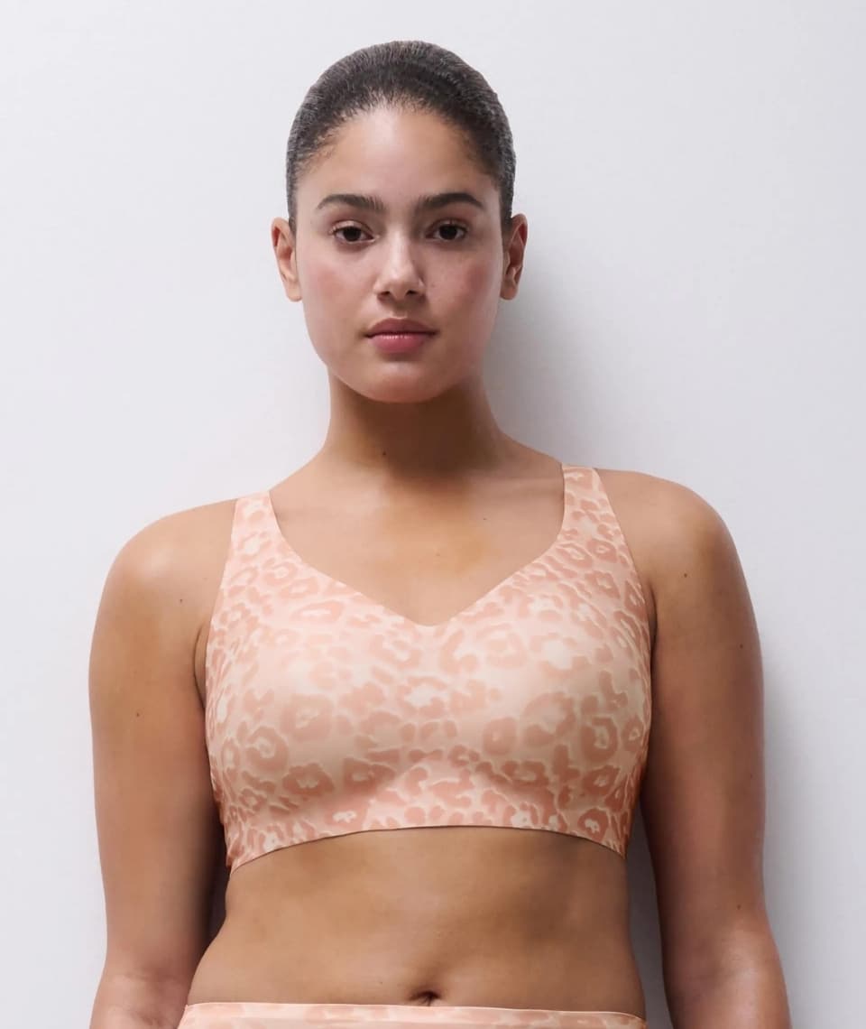 Person wearing a pink patterned bra stands against a plain white background, looking directly at the camera.