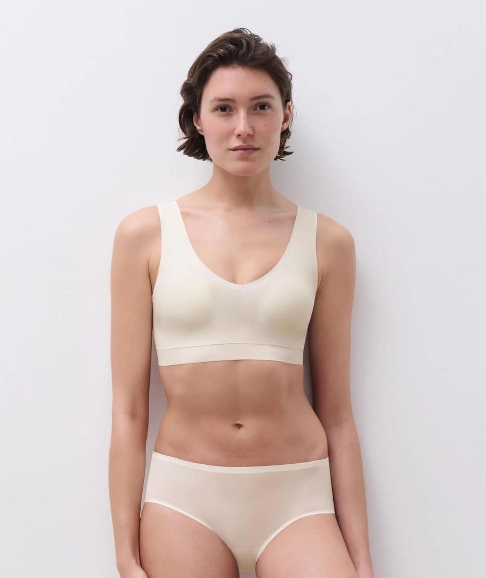 Person wearing white underwear stands against a plain white background, looking directly at the camera with a neutral expression.