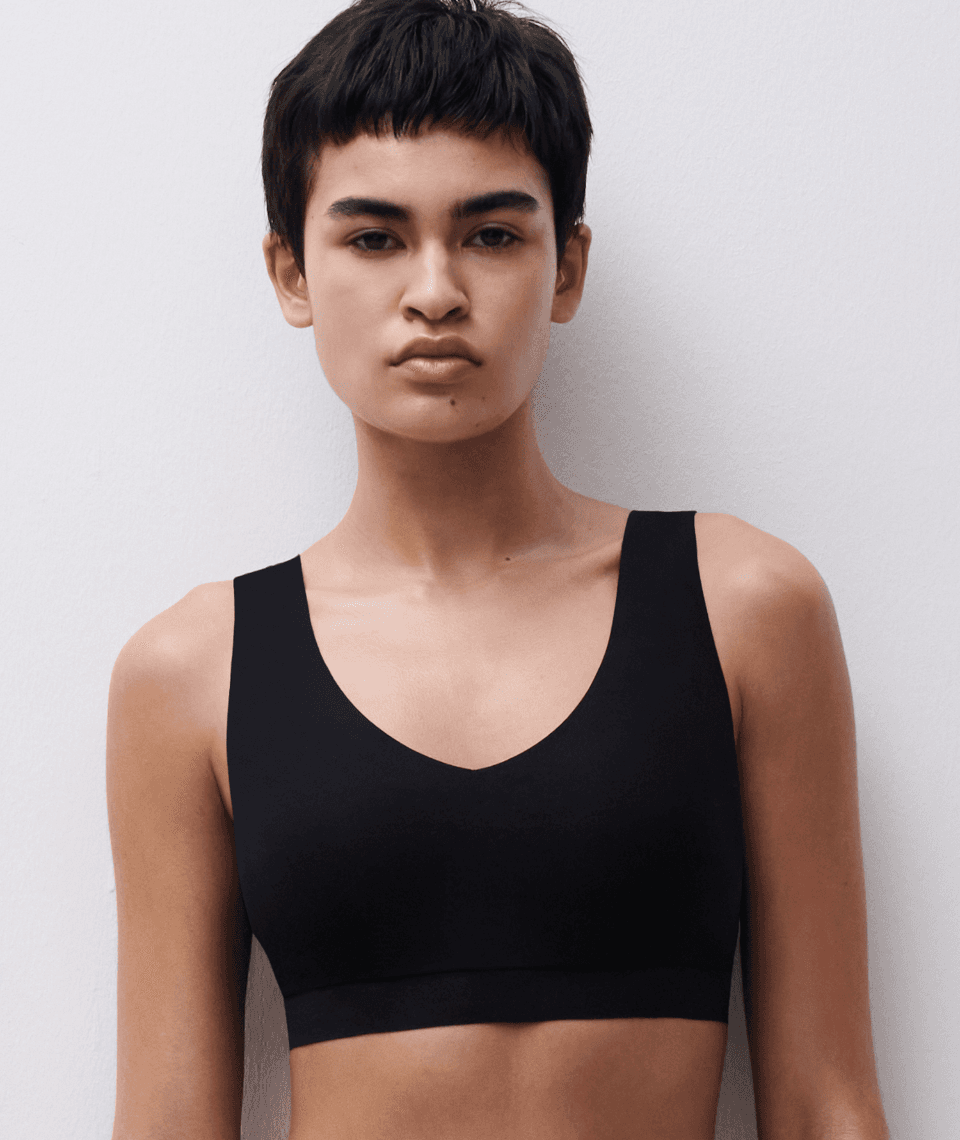Person with short hair wearing a black sleeveless top, standing against a white background.