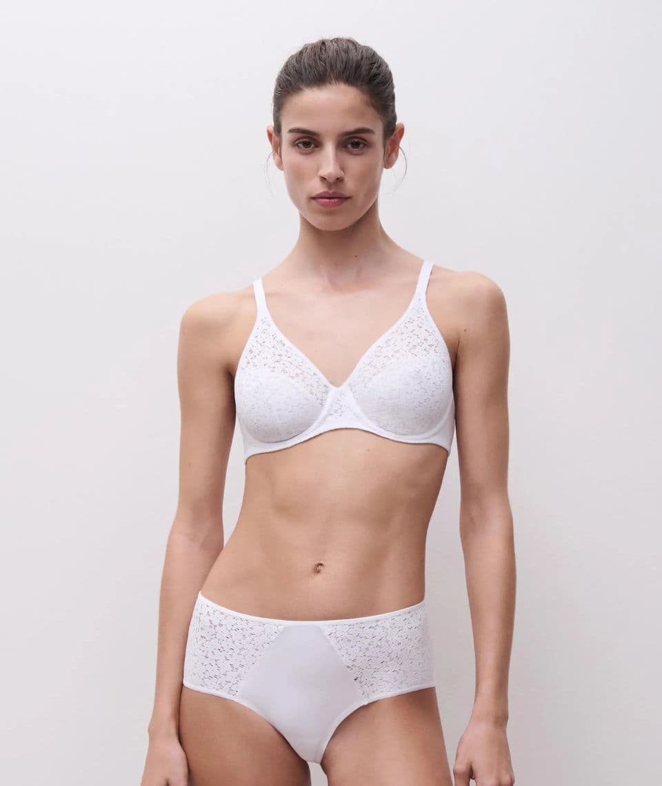 A person wearing a white lace bra and panties, standing against a plain light background.
