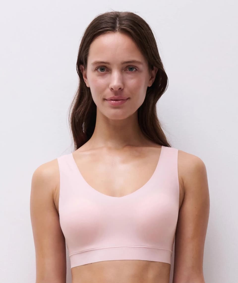 Person wearing a soft pink seamless bra, standing infront of a grey wall