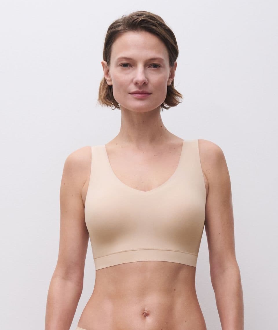Person wearing a beige seamless bralette, standing against a plain white background.