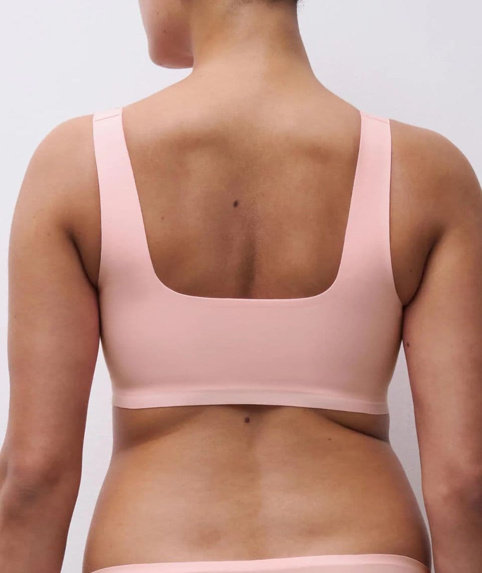 A person wearing a pink bra viewed from the back against a plain white background.