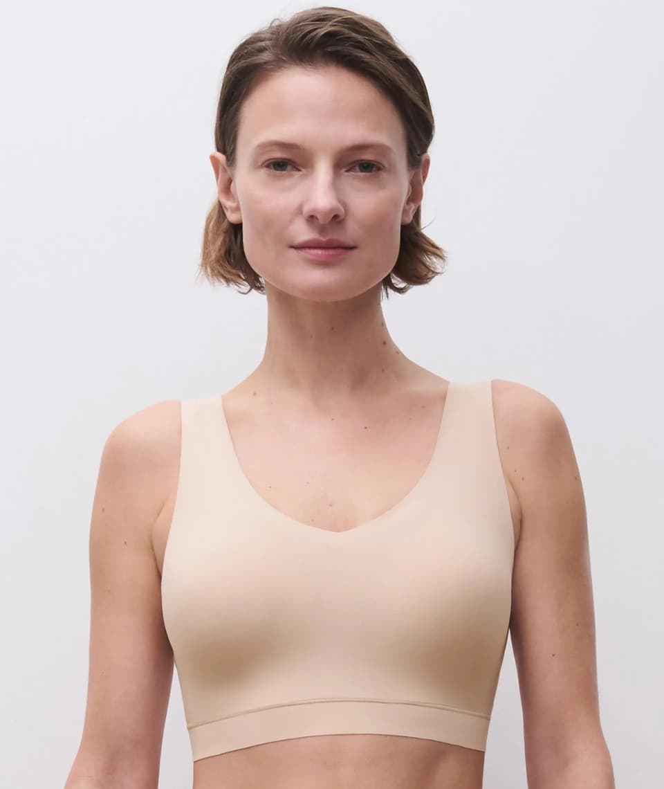 Person wearing a beige seamless bra, standing against a plain white background, looking directly at the camera.