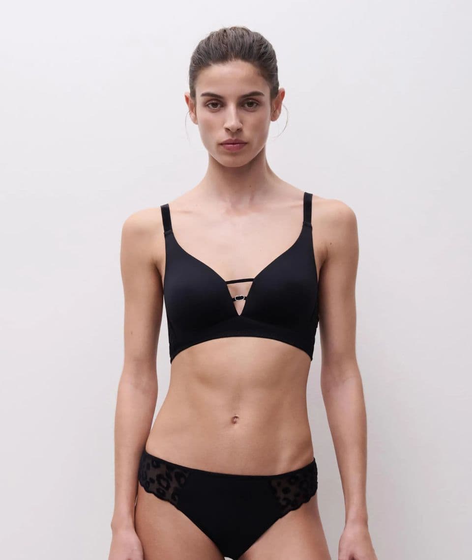 Woman wearing a black bra with decorative straps and matching bottoms, standing against a plain white background.