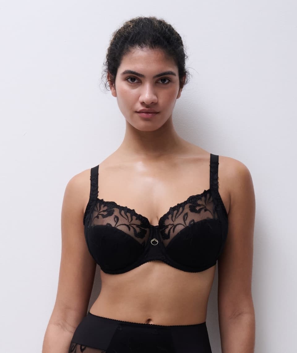 Person wearing a black lace bra with floral patterns, standing against a plain white background.