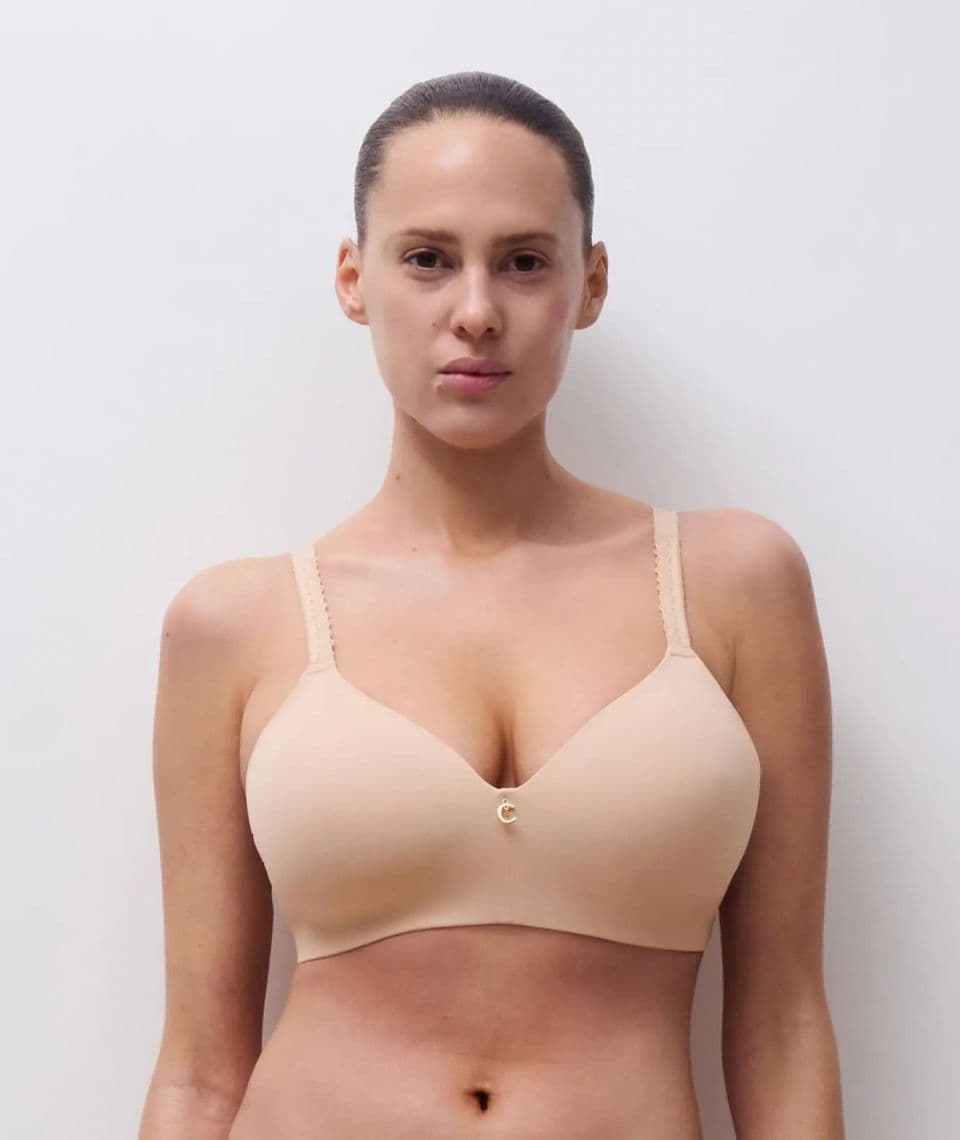 Person wearing a beige bra with a small decorative element in the center, standing against a plain white background.