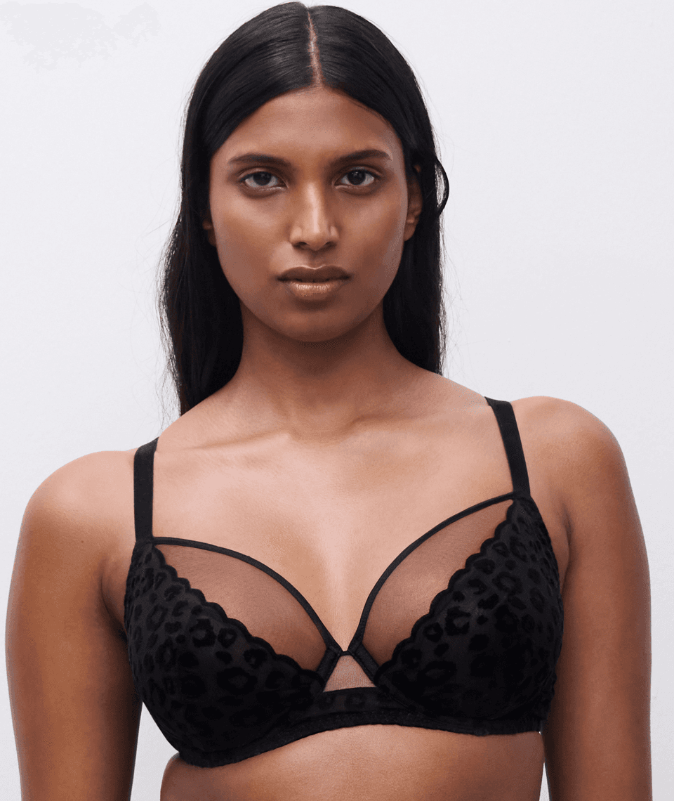 A person with long, dark hair models a black leopard-print bra with sheer panels and thin straps against a neutral background.