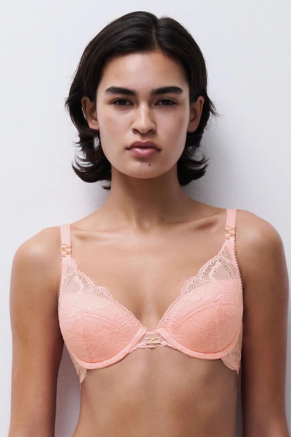 Person wearing a peach-colored lace bra, standing against a plain white background.