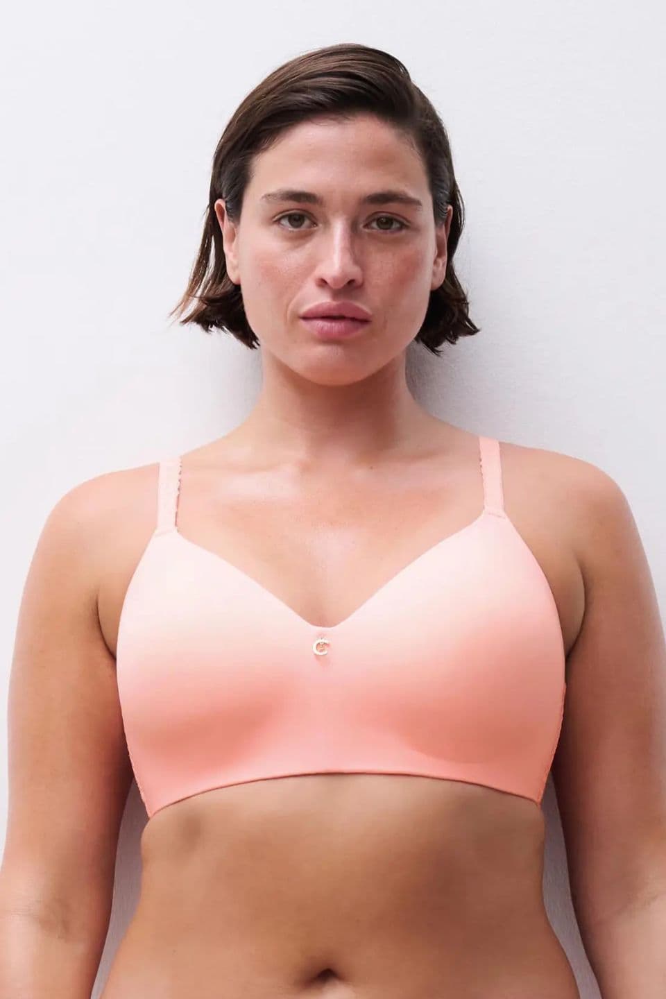 Person wearing a peach-colored bra with a minimal design, standing against a plain white background.
