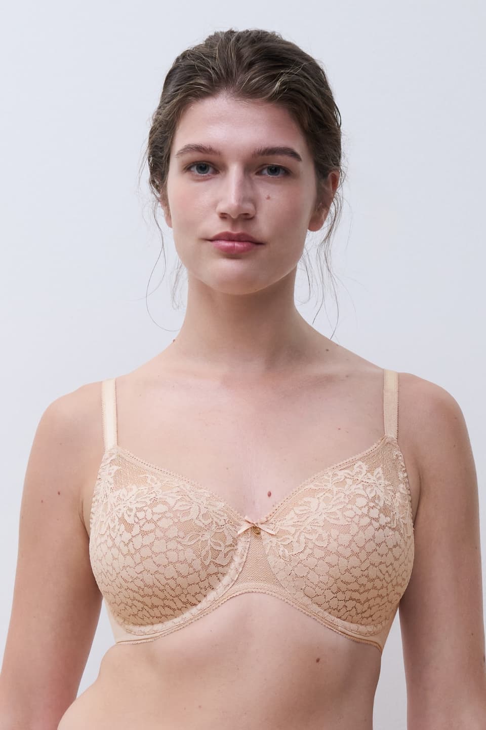 Person wearing a beige lace bra with a subtle floral pattern, standing against a plain white background.