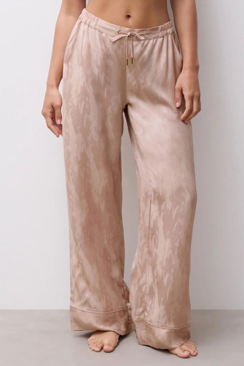 A woman is seen wearing wide-leg pyjama pants in a silky beige fabric