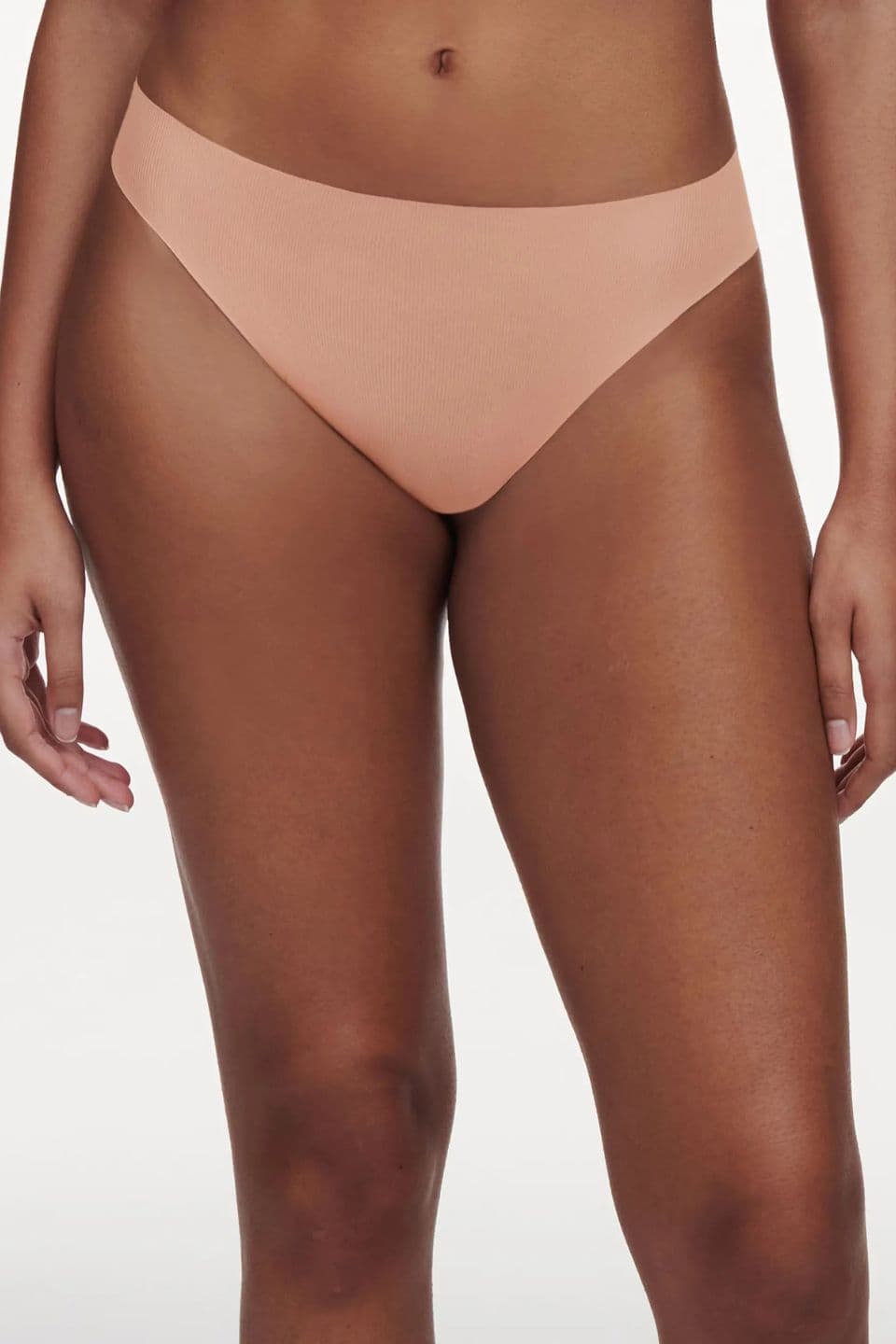 The image shows a close-up of a woman wearing a peach-colored seamless thong with a smooth, invisible finish.
