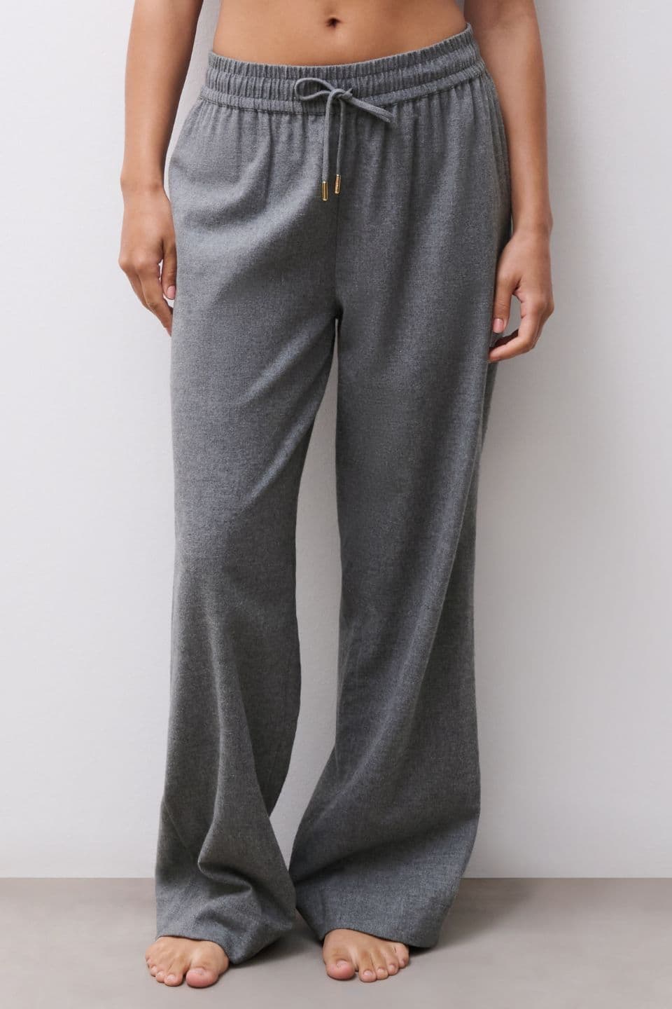 The image shows a woman wearing relaxed grey lounge pants with a soft, wide-leg fit and an adjustable drawstring waist.
