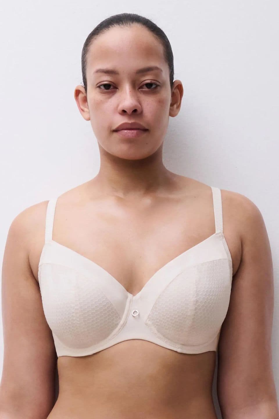 Person wearing a beige textured bra, standing against a plain white background, looking directly at the camera.