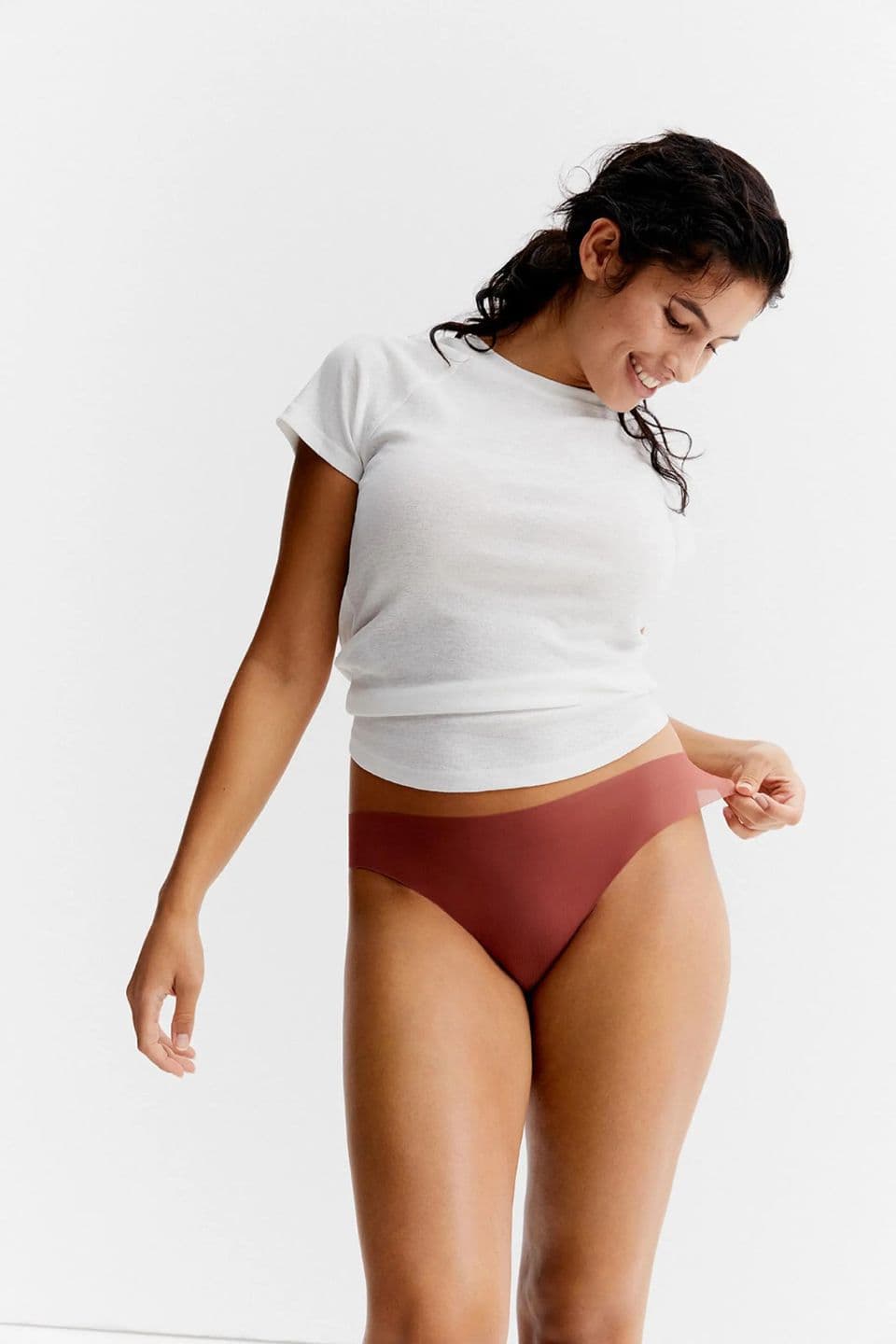 The image shows a woman wearing a sienna-colored thong and a white T-shirt.