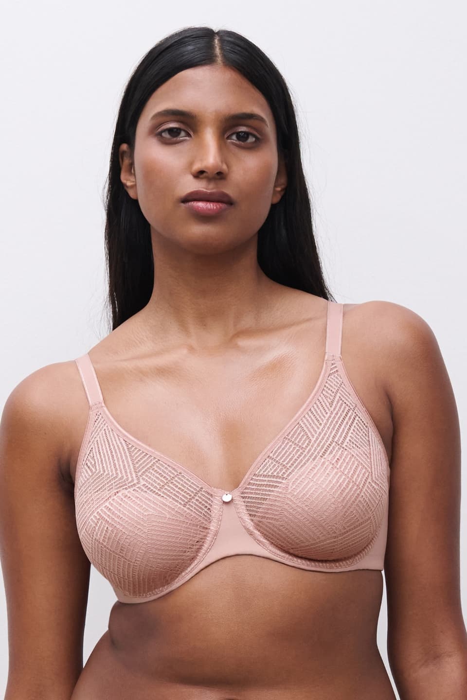 A person wearing a nude-colored bra with geometric lace patterns, standing against a plain white background.