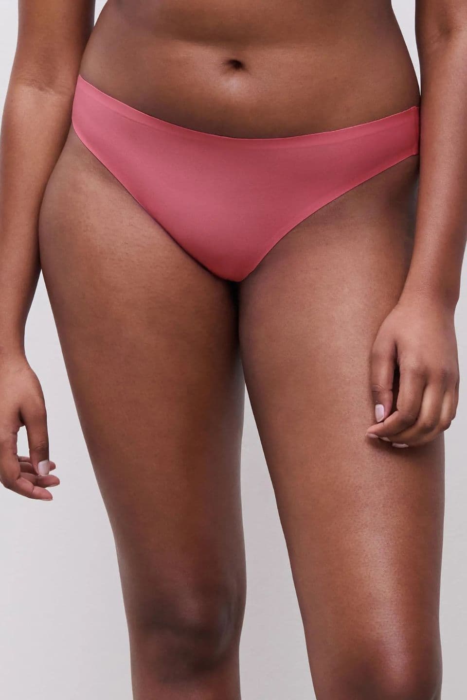 The image shows a close-up of a woman wearing a seamless brief in a soft rose color, designed for a smooth, invisible look under clothing.