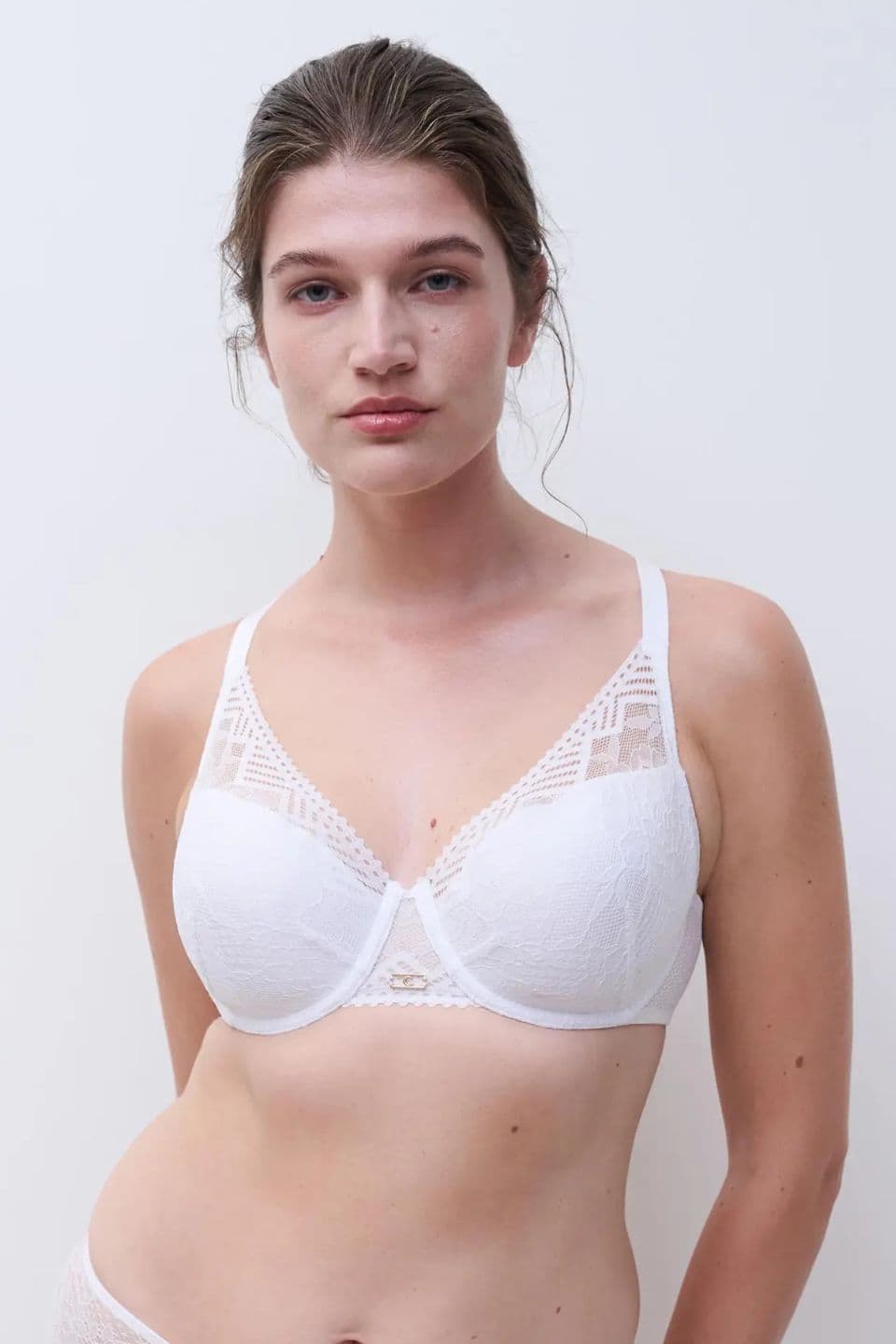Person wearing a white lace bra with geometric patterns, standing against a plain background.