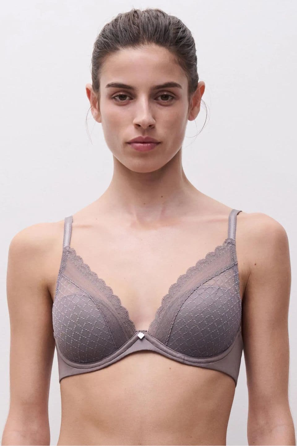The image shows a woman wearing a taupe lace bra with delicate scalloped edges and subtle geometric embroidery, creating a soft and refined look.