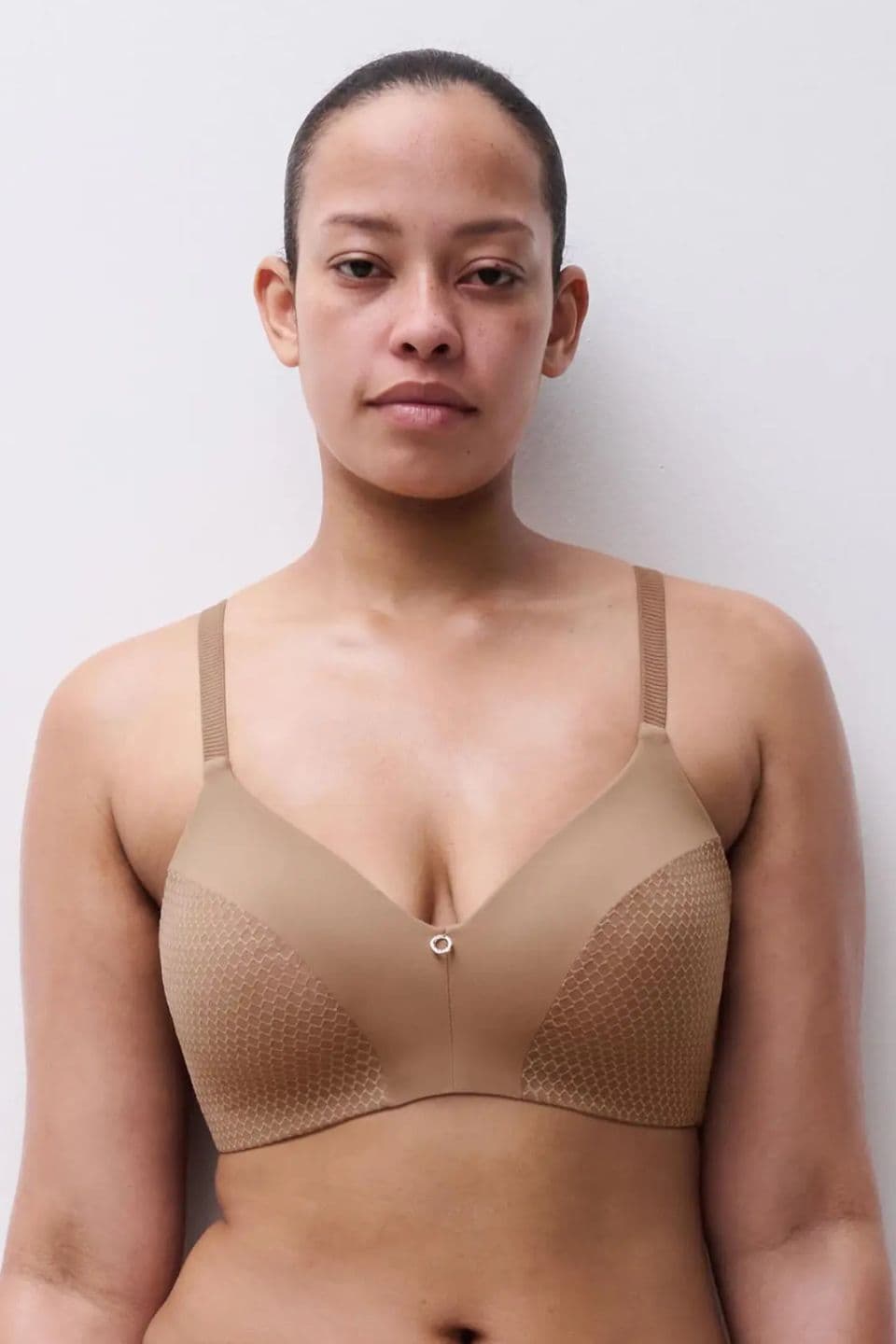 Person wearing a beige bra with a subtle pattern, standing against a plain white background.