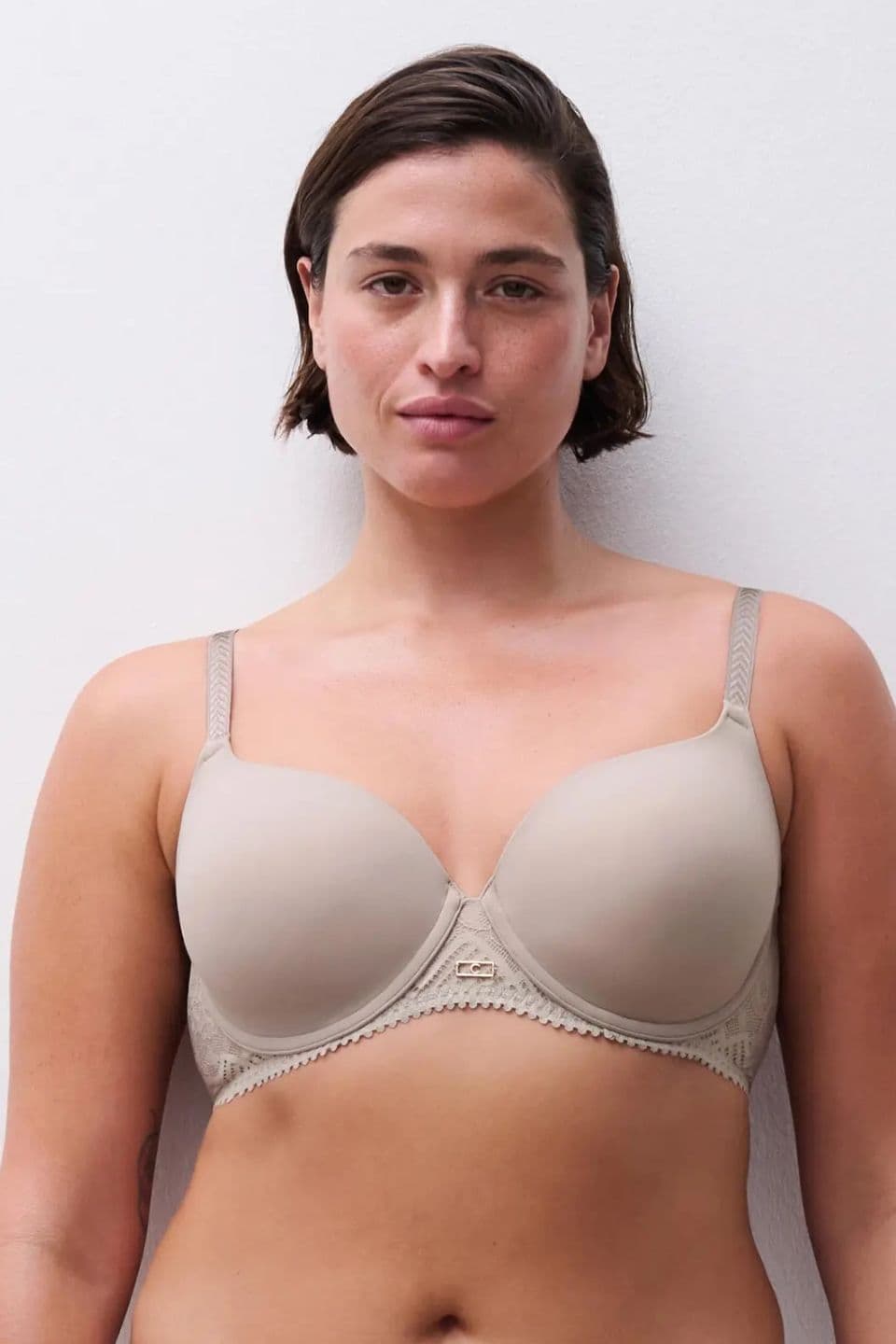 Person wearing a grey bra stands against a plain white background, looking directly at the camera.