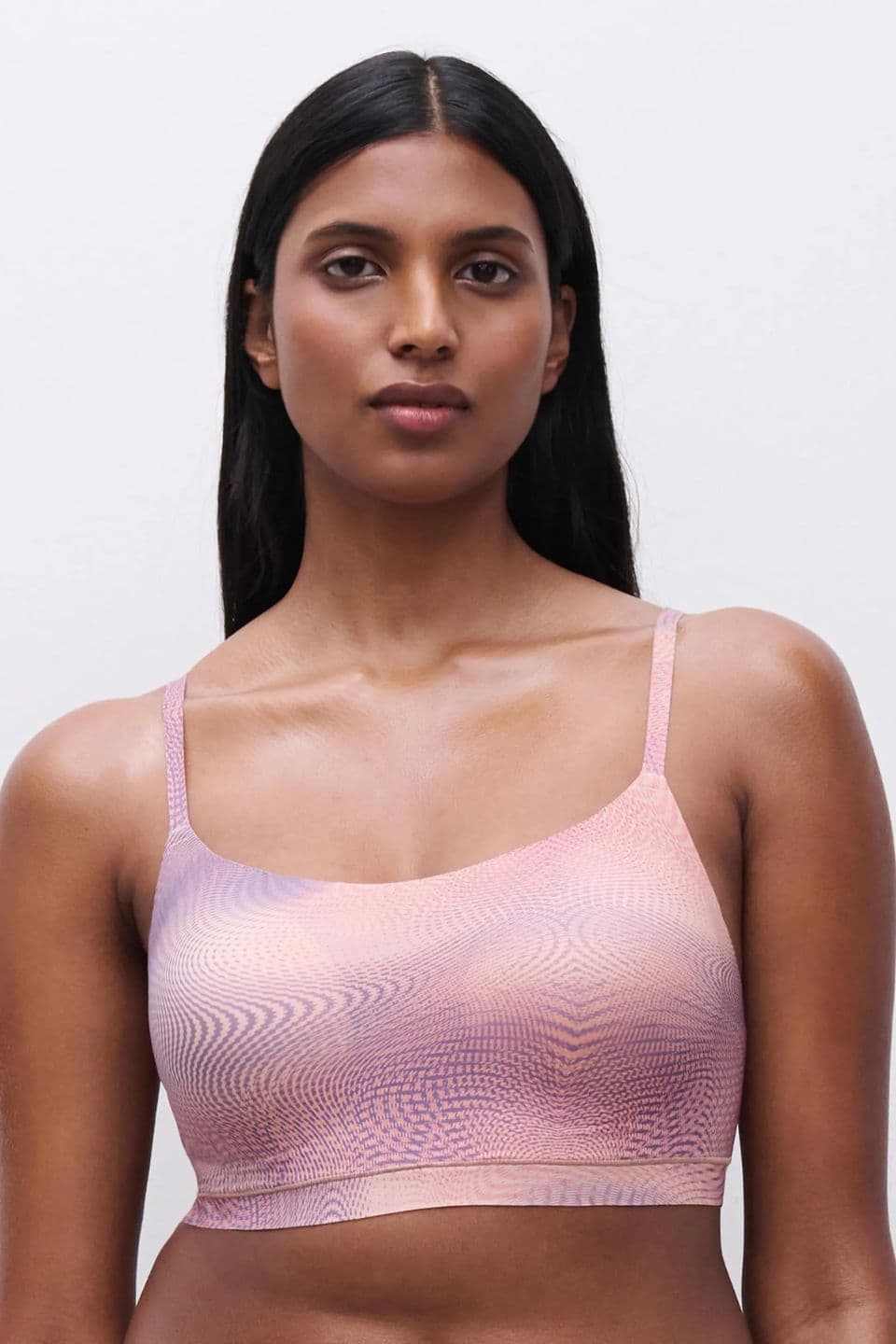 The image shows a woman wearing a seamless SoftStretch bra in a pastel, wavy print for a smooth and comfortable look