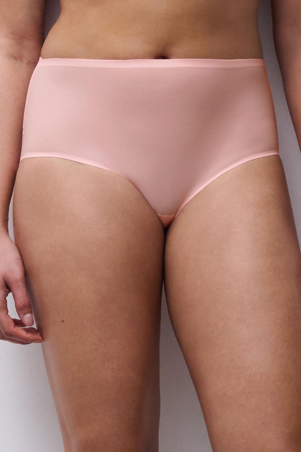 A person wearing high-waisted, light pink underwear stands against a white background, with their arms relaxed by their sides.