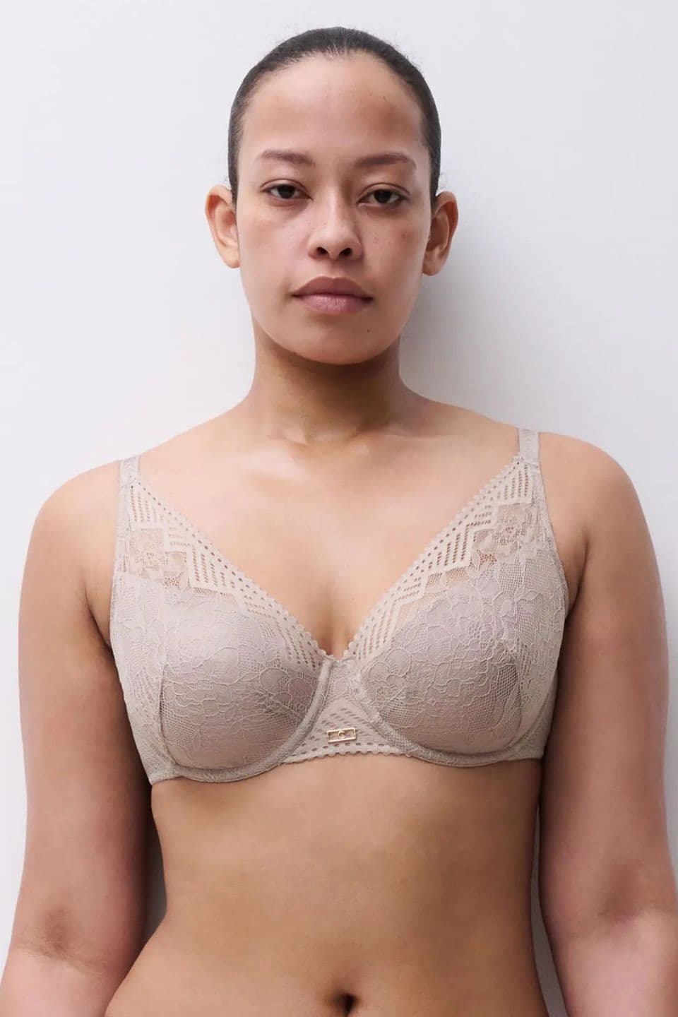 Person in a beige lace bra standing against a plain white background, looking directly at the camera.