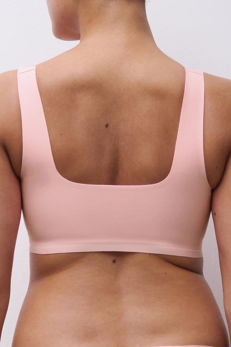 Person wearing a light pink square-neck bra, showing back and shoulders against a plain background.