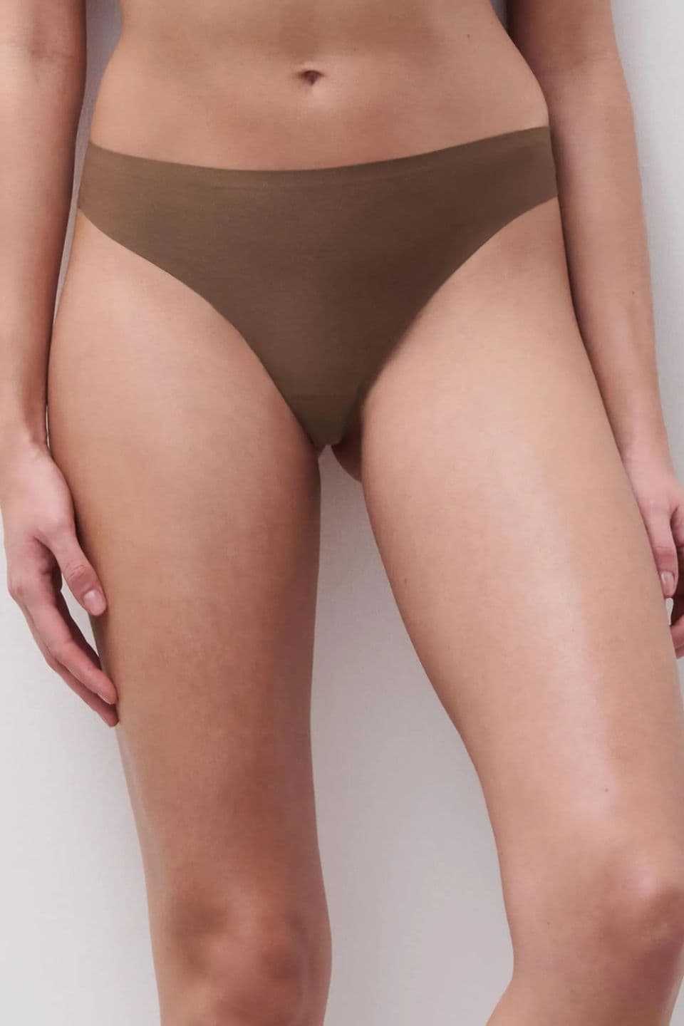 The image shows a close-up of a woman wearing a seamless brief in a brown color, designed for a smooth, invisible look under clothing.