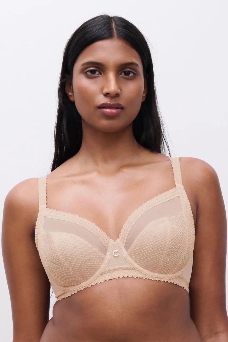 A person wearing a beige, textured bra with sheer paneling stands against a neutral background.