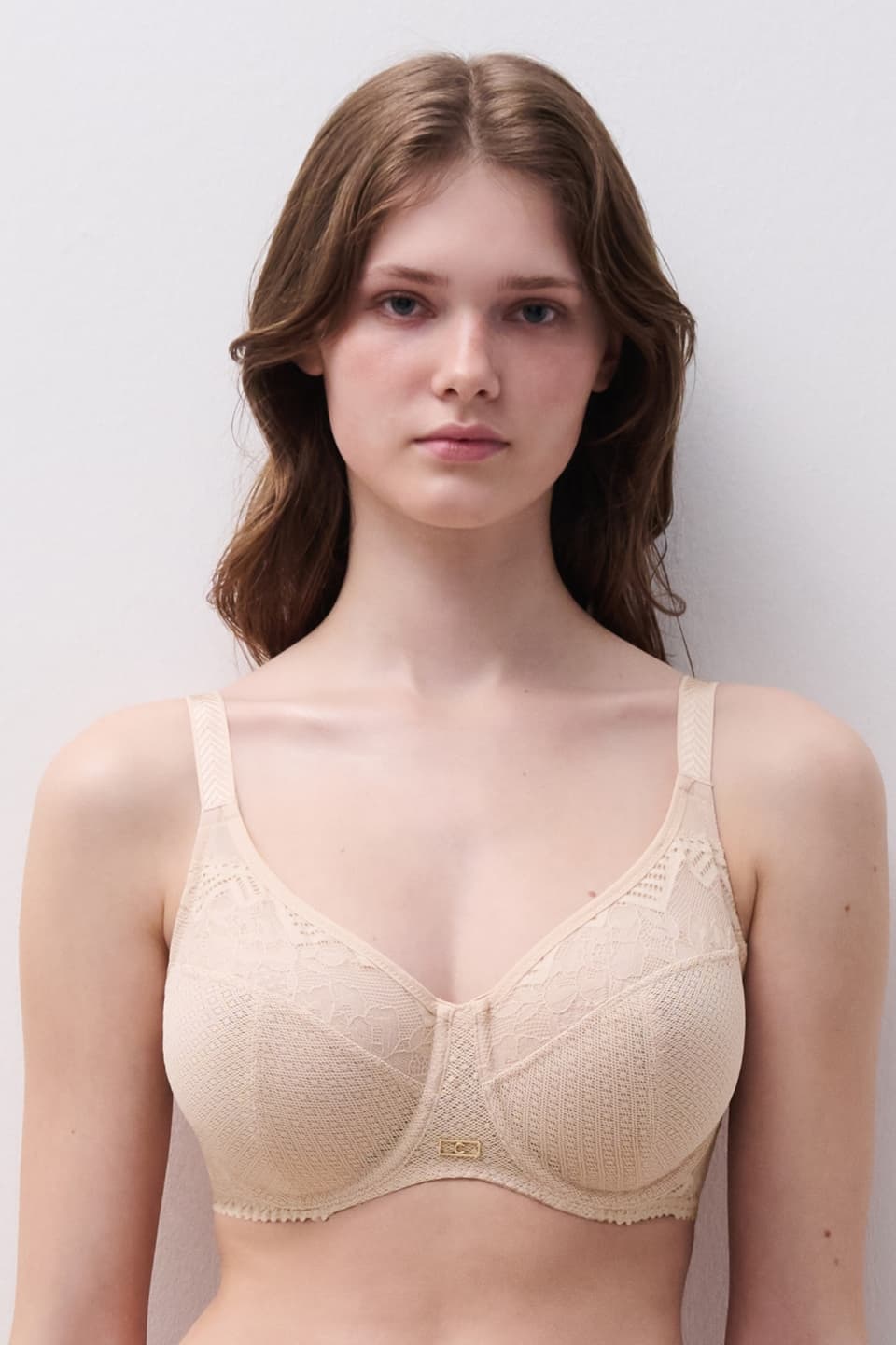 Woman wearing a beige lace bra, standing against a plain white background.