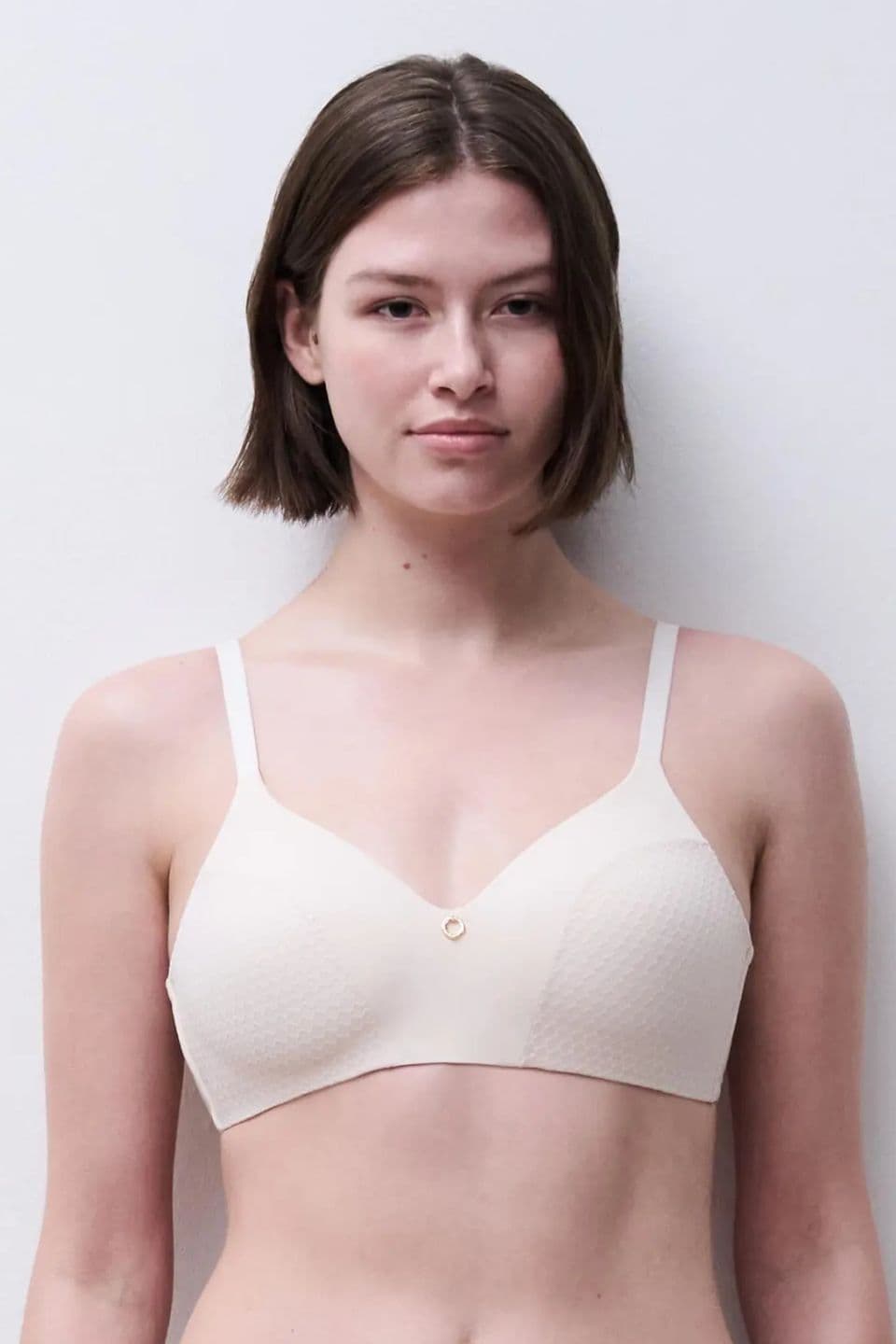 A person wearing a white, textured bra standing against a plain white background. The bra features thin straps and a small button detail in the center.