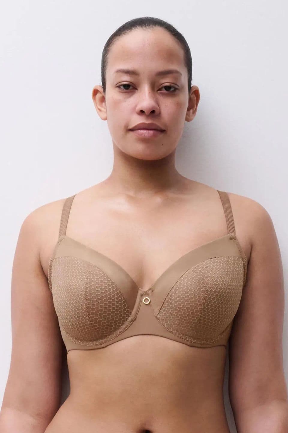 A person wearing a beige bra stands against a plain white background, looking directly at the camera with a neutral expression.