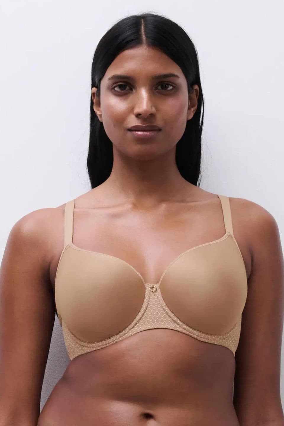 Person wearing a beige bra, standing against a plain white background, with straight hair and a neutral expression.