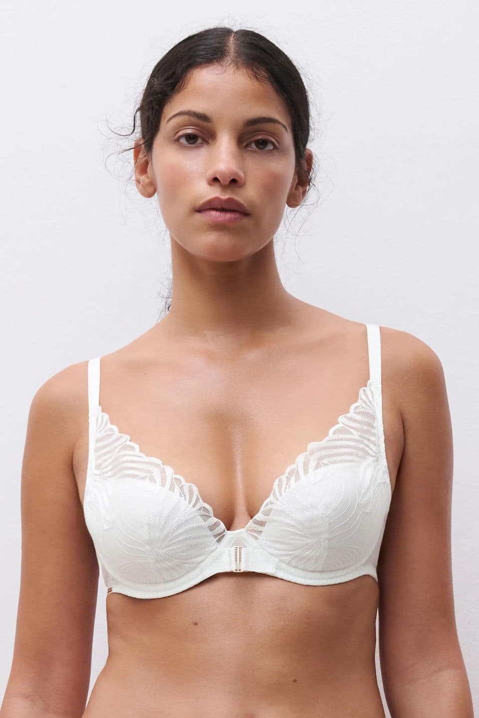 A person wearing a white lace bra with intricate patterns stands against a plain background.
