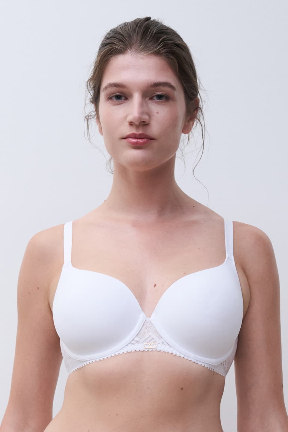 A person wearing a white bra with thin straps stands against a plain background.