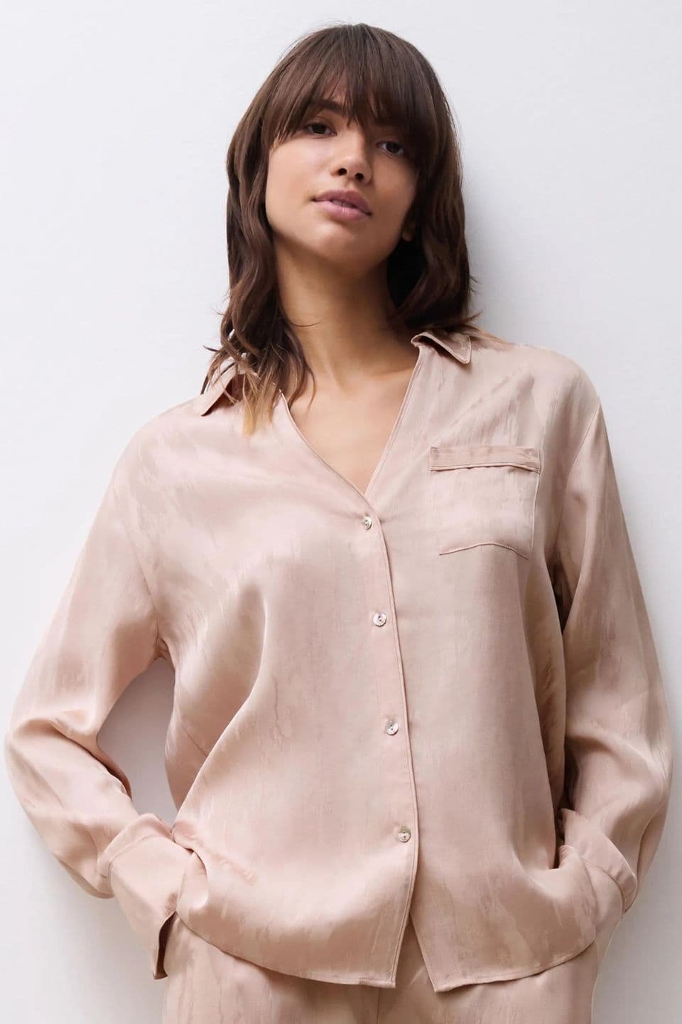 The image shows a woman wearing a soft, satin-look pyjama shirt in a light beige shade.