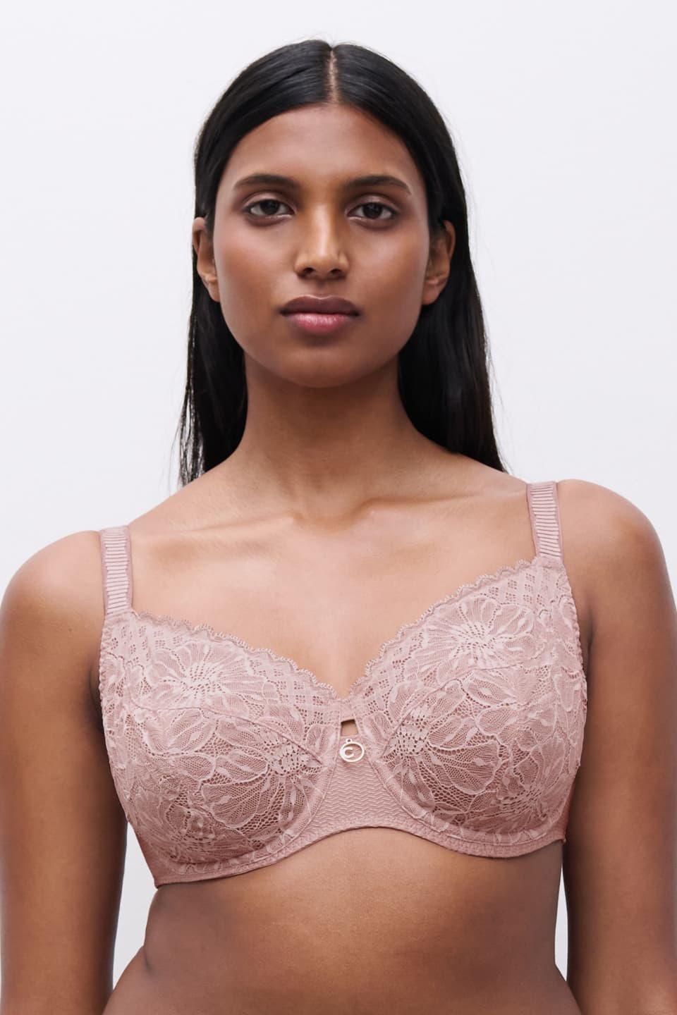 Woman wearing a pink lace bra with floral patterns, standing against a plain white background.