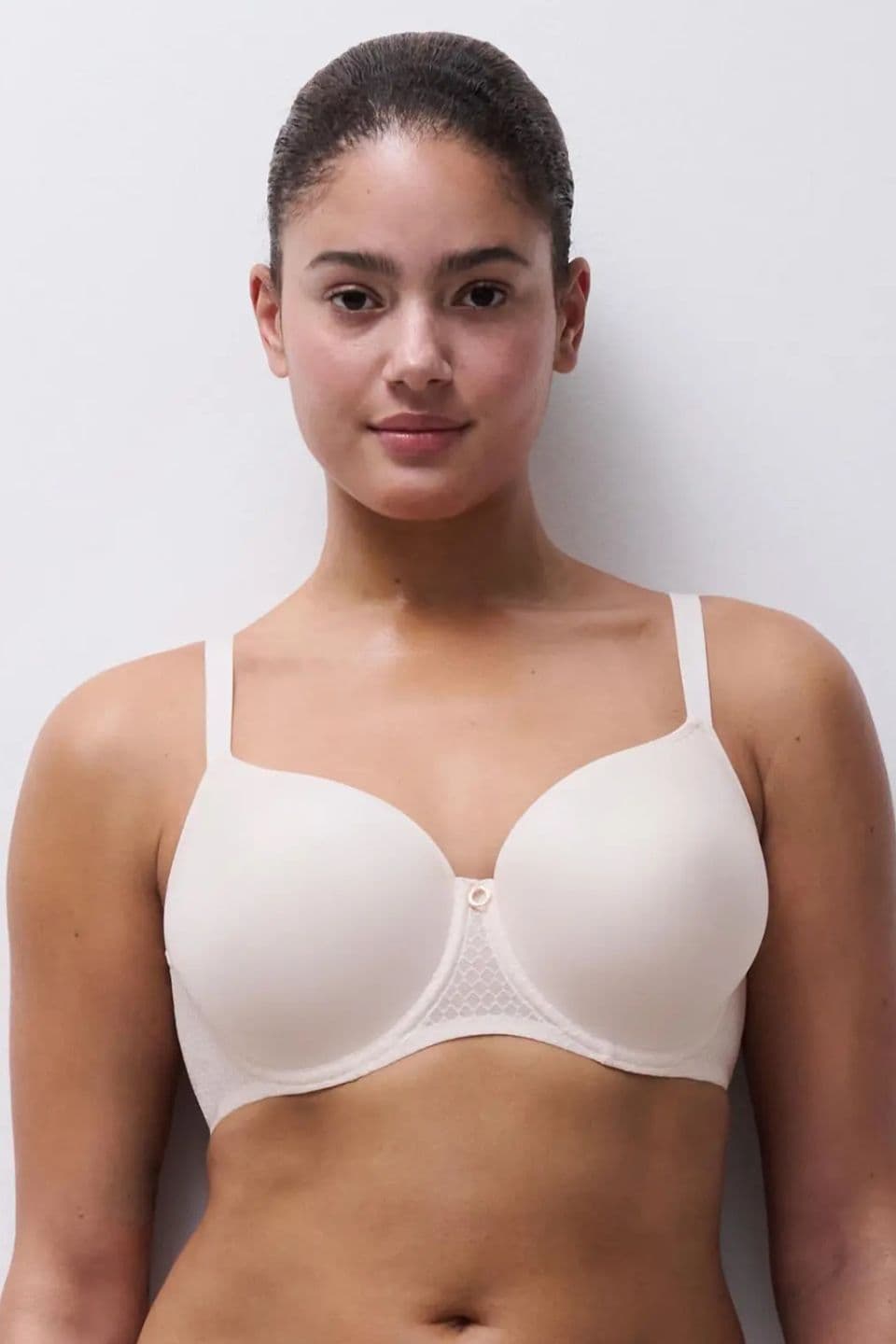 A person wearing a white bra stands against a plain white background, facing forward with a neutral expression.