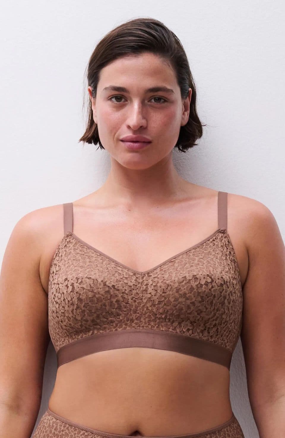 Person wearing a brown, leopard-patterned bralette with thin straps, standing against a plain white background.
