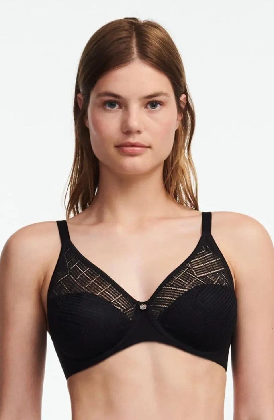 A woman wearing a black bra with lace detail stands against a plain background.