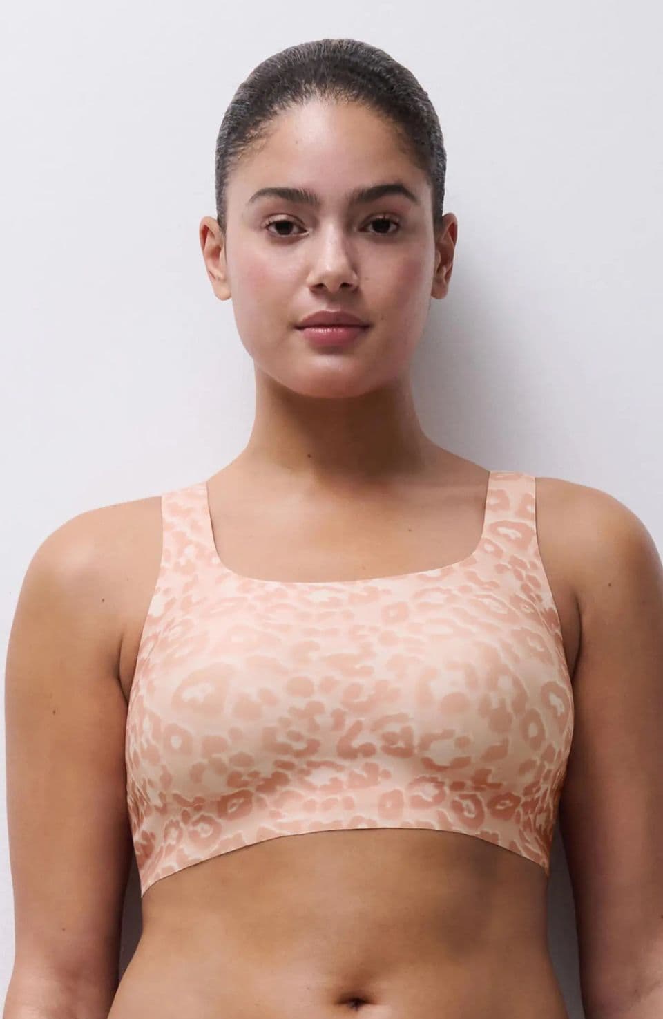 Woman wearing a beige, leopard-print sports bra, standing against a plain white background.
