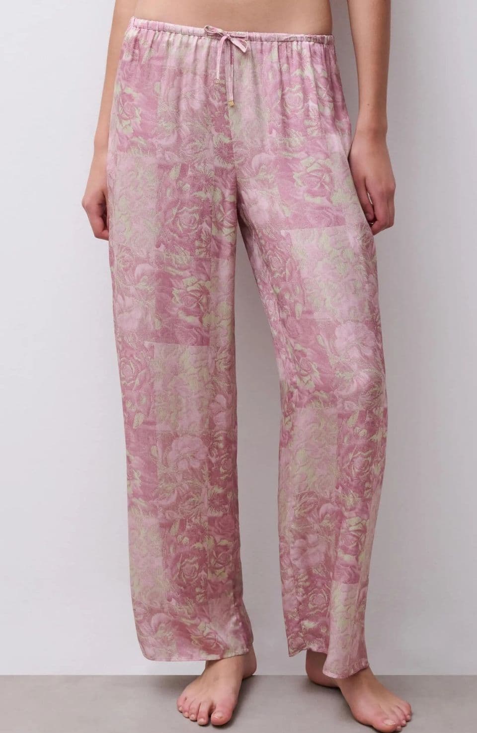 Person wearing loose, pink floral pajama pants with an elastic waistband, standing barefoot against a plain background.