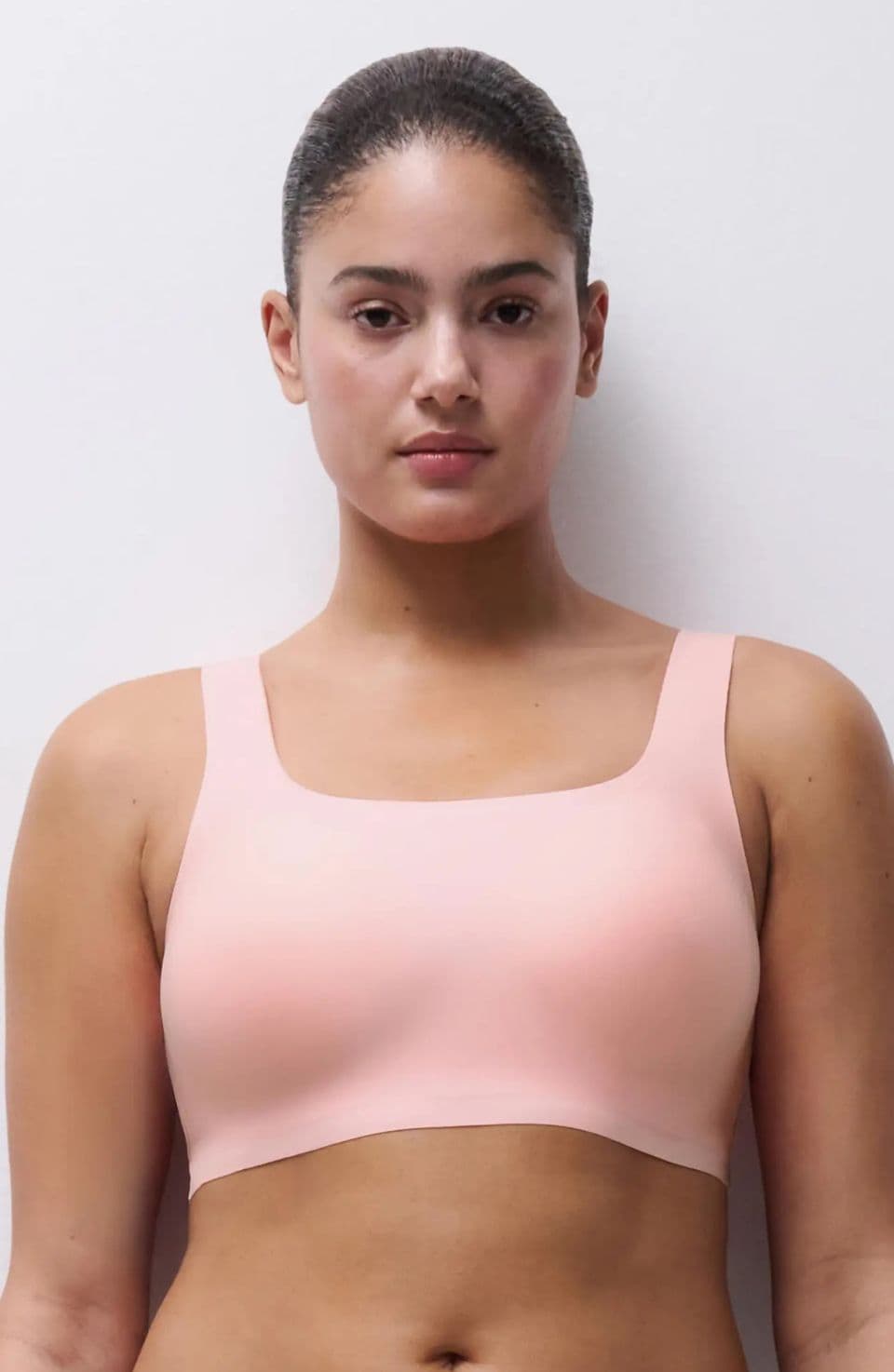 A person wearing a peach-colored seamless sports bra stands against a plain white background.