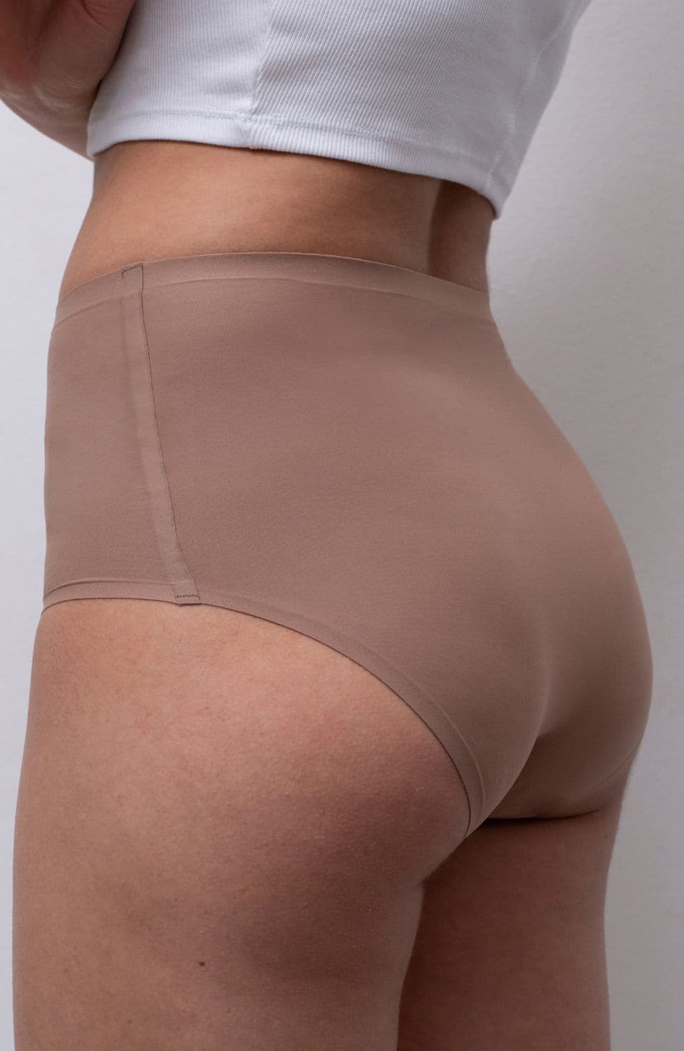 SoftStretch in beige Person wearing a beige, seamless undergarment and a white top, standing against a plain background.